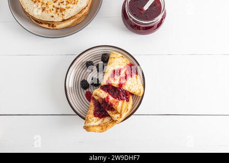 Blick von oben auf den Teller mit frisch geschnittenen Crepes, Pfannkuchen mit Marmelade und Beeren auf weißem Holztisch. Ein Kopierbereich. Leckeres Frühstück. Nachtisch Stockfoto