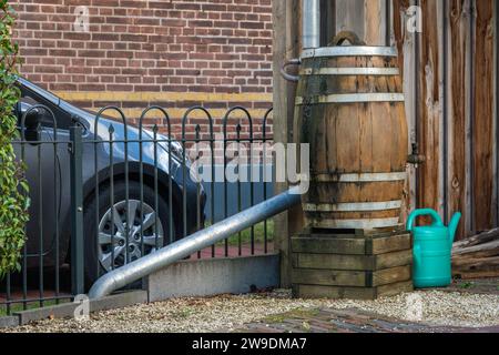 Regenfass und Gießkanne vor einem modernen Haus, Regenwassertank zur Regenwassergewinnung und -Wiederverwendung Stockfoto