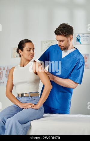 Attraktive junge Frau in lässiger Kleidung beobachten, wie Doktor ihre Schulter überprüft, Gesundheit Stockfoto
