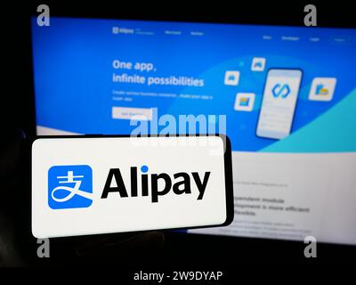 Person, die ein Smartphone mit dem Logo des chinesischen Zahlungsplattform-Unternehmens Alipay vor der Website hält. Schwerpunkt auf dem Display des Telefons. Stockfoto