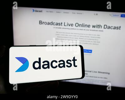Person, die ein Mobiltelefon mit dem Logo des Live-Video-Streaming-Unternehmens Dacast Inc. Vor der Unternehmenswebseite hält. Schwerpunkt auf dem Display des Telefons. Stockfoto