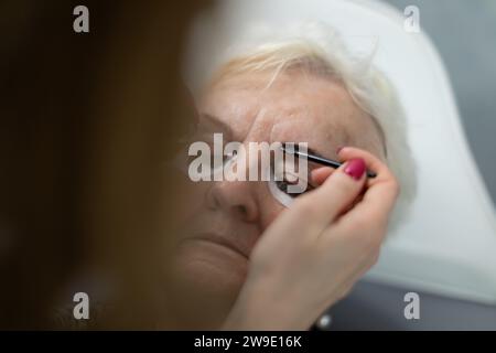 Eine Kosmetikerin trägt ein schwarzes Farbprodukt auf die Augenbrauen eines Schönheitssalons auf. Stockfoto