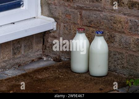 Doorstep Milchlieferung GB. Ein Pint Magermilch und ein Pint halbMagermilch in Glasflaschen vor der Haustür, die ein Milchmann in Großbritannien hinterlassen hat. Stockfoto