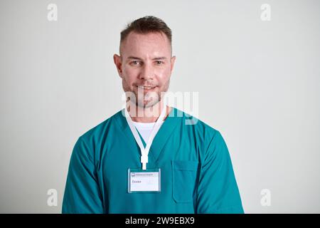 Porträt eines lächelnden Reifen Arztes mit Abzeichen, der grüne Peelings trägt Stockfoto