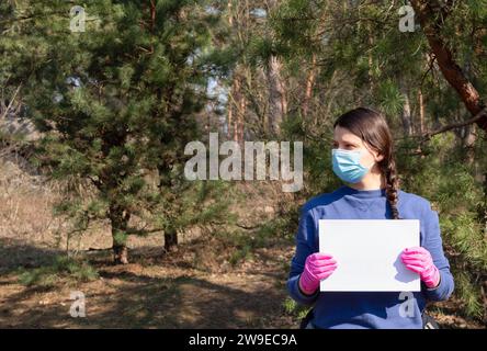 Ein Mädchen in einer Schutzmaske und Handschuhen hält ein leeres Blatt Papier für Text. Gefährliche tödliche Epidemie der nCoV Stockfoto