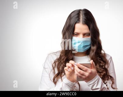 Covid-19. Mädchen mit Schutzmaske schreibt eine Nachricht in ein Smartphone. Pandemie des Coronavirus. Epidemie der nCoV. Stockfoto