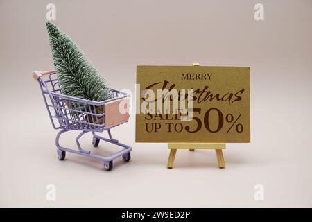 Weihnachtsangebot 50 % Rabatt auf Textnachricht mit Miniatur-Modell Winterkiefer auf Einkaufswagen auf rosa Hintergrund Stockfoto