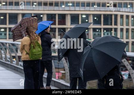 Menschen trotzen dem Wetter, wenn sie die Millennium Bridge in London überqueren. Sturm Gerrit wird am Mittwoch starke Winde und starke Regenfälle in viele Teile Großbritanniens bringen, wobei auch winterliche Gefahren wahrscheinlich sind, warnten die Wettervorhersagen. Bilddatum: Mittwoch, 27. Dezember 2023. Stockfoto