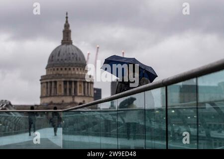 Menschen trotzen dem Wetter, wenn sie die Millennium Bridge in London überqueren. Sturm Gerrit wird am Mittwoch starke Winde und starke Regenfälle in viele Teile Großbritanniens bringen, wobei auch winterliche Gefahren wahrscheinlich sind, warnten die Wettervorhersagen. Bilddatum: Mittwoch, 27. Dezember 2023. Stockfoto