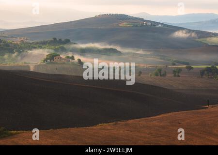 Morgennebel durch das Tal von Val d'Orcia in der malerischen Landschaft Ackerland und sanften Hügeln der ländlichen Toskana, Italien. Stockfoto
