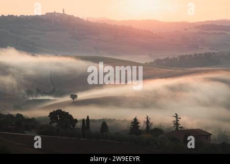 Atmosphärischer Sonnenaufgangsnebel durch das Tal von Val d'Orcia und das Dorf Pienza in der malerischen Landschaft und sanften Hügeln des ländlichen Tu Stockfoto