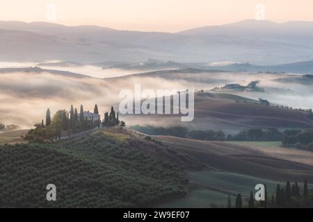 Stimmungsvoller Sonnenaufgang Nebel durch das Tal von Val d'Orcia und ein rustikales Bauernhaus in der malerischen Landschaft und sanften Hügeln der ländlichen Toskana Stockfoto