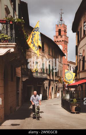 Asciano, Italien - 30. August 2023: Ein älterer italienischer Mann radelt entlang der Hauptstraße und Altstadt der malerischen und charmanten, historischen Altstadt Stockfoto