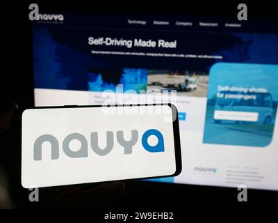 Person mit Smartphone und Logo des französischen Autonome Fahrzeugunternehmens Navya S.A. vor der Website. Schwerpunkt auf dem Display des Telefons. Stockfoto