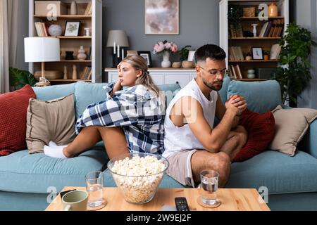 Gestresste junge verheiratete Paare sitzen getrennt auf verschiedenen Seiten des Sofas und ignorieren einander nach dem Streit. Beleidigte Ehegatten sprechen nicht Stockfoto