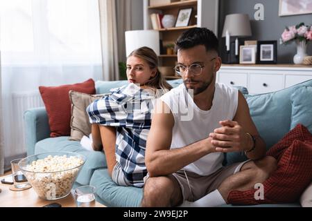 Gestresste junge verheiratete Paare sitzen getrennt auf verschiedenen Seiten des Sofas und ignorieren einander nach dem Streit. Beleidigte Ehegatten sprechen nicht Stockfoto