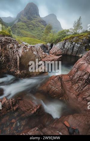 Moody, stimmungsvolle Berglandschaft entlang des Flusses Coe zu den Three Sisters of Glencoe in den schottischen Highlands. Stockfoto