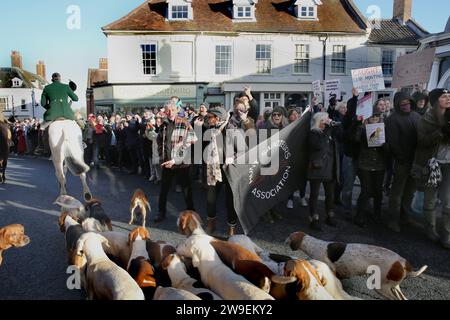 Jagd-Demonstranten schwenken Plakate, während die Reiter und Hunde während der Jagdparade am zweiten Weihnachtsfeiertag vorbeifahren. Im Stadtzentrum von Bungay wurde Protest gegen Tierquälerei abgehalten, als die Waveney und Norfolk Harriers durch die Straßen ziehen und die Landsleute unterstützen. Die Demonstranten sagten, dass trotz ihres Verbots der traditionellen Fuchsjagd Tiere immer noch während der Wanderjagd getötet werden und sie fordern ein totales Verbot. Stockfoto