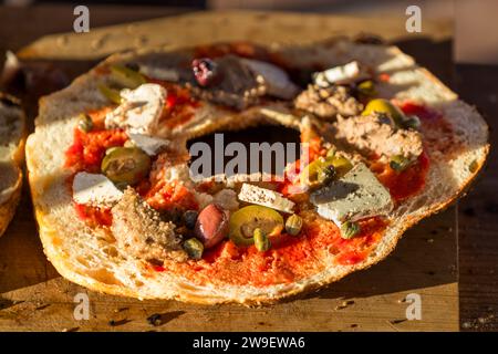 Ein vollständig belegtes ringförmiges Ftira-Fladenbrot mit Tomatensauce, ġbejna-Käse, Oliven, Kapern und Thunfisch ist bereit für den Holzofen im Girgenti Olive Grove in Siġġiewi, Malta, wo Besucher es selbst backen. Die traditionelle maltesische Ftira wurde 2020 in die UNESCO-Liste des immateriellen Kulturerbes aufgenommen. Stockfoto