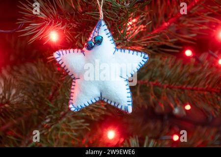 Hausgemachte, handgemachte Weihnachtsbaumschmuck auf einem Baum mit Lichtern, einem weißen Stern Stockfoto