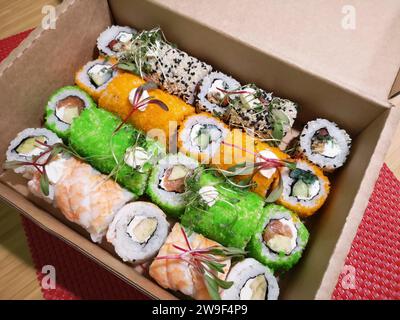 Eine appetitliche Auswahl an Sushi-Brötchen, die in einem Karton auf einem roten Tischset angeordnet sind Stockfoto