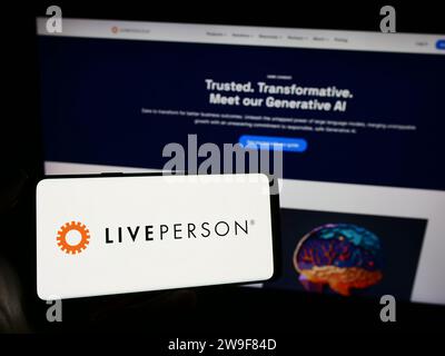 Person, die ein Mobiltelefon mit dem Logo des Konversationsunternehmens LivePerson Inc. Vor der geschäftlichen Webseite hält. Schwerpunkt auf dem Display des Telefons. Stockfoto