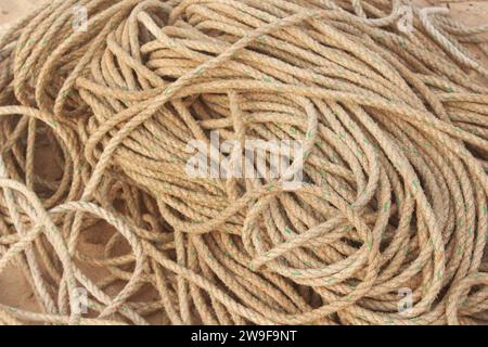 Eine dicke Spule aus verwittertem Seil sitzt auf einem sonnengebleichten Holzdock. Die Textur des Seils ist rau und abgenutzt, die Farben verblassten zu Braun- und Grautönen Stockfoto