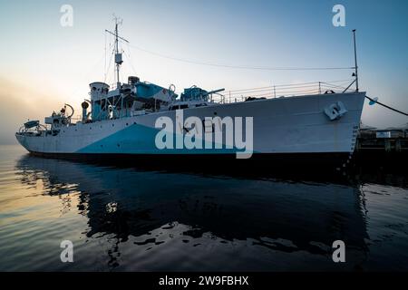 Museumsschiff HMCS Sackville reflektiert auf ruhigem Wasser bei Sonnenaufgang an einem nebeligen Morgen an der Uferpromenade in Halifax, NS. Stockfoto