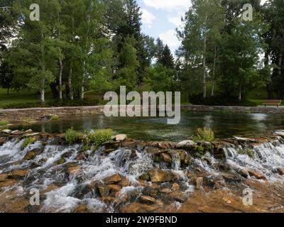Blick auf das Wasser, das über Steine von Giant Springs in Great Falls, Montana fließt, mit Giant Springs Park im Hintergrund. Stockfoto