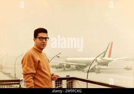 Ein junger Mann posiert auf der Terrasse des Flughafens Malpensa (Mailand) mit einer Alitalia Douglas DC8 im Hintergrund Ende der 60er Jahre. Stockfoto