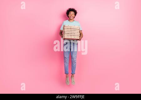 Foto in voller Größe von nettem jungen Mann springt Pizzaboxen tragen trendiges blaues Outfit isoliert auf rosa Hintergrund Stockfoto