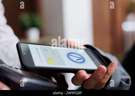 Nahaufnahme von Touristen, die kontaktlos per Mobiltelefon mit NFC-Technologie bezahlen. Detaillierte Ansicht von zwei Händen, die Pos Terminal und Smartphone greifen, bezahlende Winterurlaub-Reservierung. Stockfoto