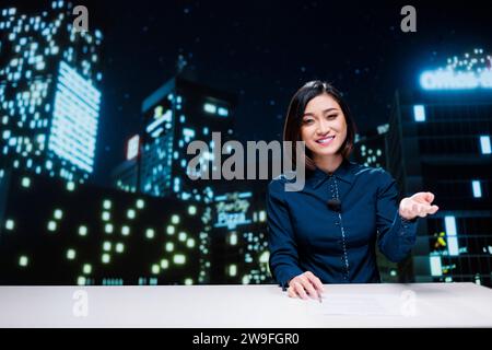 Moderator geht live über die Übertragung in das Nachrichtensegment für internationale Fernsehsendungen und nutzt Schlagzeilen von Medienanstalten. Asiatische Reporterin moderiert Nachtshow, um über Ereignisse zu sprechen. Stockfoto