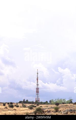 Minimalistische Fotografie der Telekommunikationsantenne in vertikaler Ebene, mit negativem Raum oben, blauem Himmel und grünem Feld rund um die Natur Stockfoto