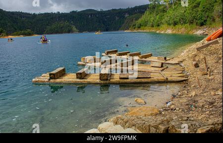 Ruhe am See: Hölzerner Pier auf einem Chiapas See, azurblaues Wasser, üppige Bäume, Erdboden, ferne Boote, Bedeckter Tag. Montebello's Lake. Stockfoto