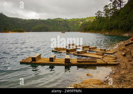 Ruhe am See: Hölzerner Pier auf einem Chiapas See, azurblaues Wasser, üppige Bäume, Erdboden, ferne Boote, Bedeckter Tag. Montebello's Lake. Stockfoto