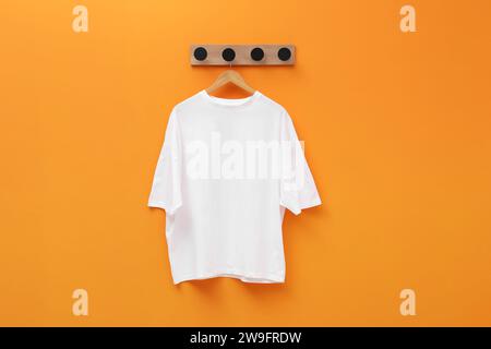 Kleiderbügel mit weißem T-Shirt an der orangefarbenen Wand Stockfoto