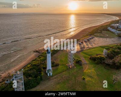 Aus der Vogelperspektive eines Sonnenuntergangs über einem Küstenparkplatz und Leuchtturm bei Queenscliff auf der Bellarine Peninsula in Victoria, Australien. Stockfoto