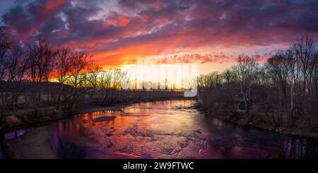 Ein lebhafter und farbenfroher Sonnenuntergang über dem flachen Wasser des White River in der Nähe von Seymour, IN. Viele warme Farben; Orange und Gelb, blaue Schatten Stockfoto