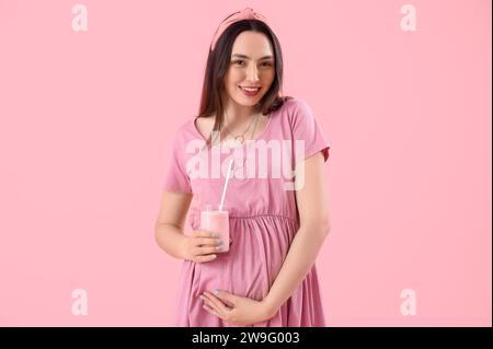 Junge schwangere Frau mit einem Glas Smoothie auf pinkfarbenem Hintergrund Stockfoto