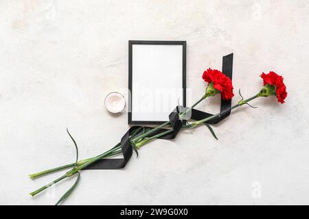 Leerer Trauerrahmen, brennende Kerze und Nelkenblumen auf hellem Hintergrund Stockfoto