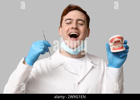Männlicher Zahnarzt mit Zahnforscher und Kiefermodell auf grauem Hintergrund. Weltzahnarzttag Stockfoto