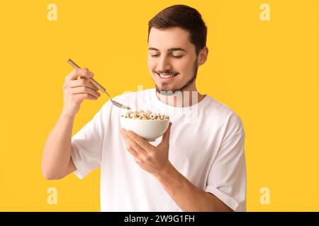 Schöner junger Mann, der leckere Müsliringe auf gelbem Hintergrund isst Stockfoto