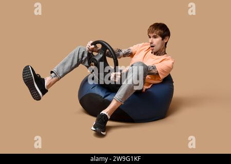 Emotionaler junger Mann mit Lenkrad auf beigefarbenem Hintergrund Stockfoto