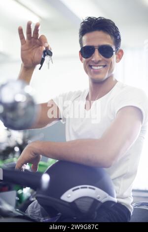 Gutaussehender Mann, Porträt- und Motorradschlüssel mit Helm und Sonnenbrille für Transportfahrzeuge in der Garage. Junge männliche Person oder Biker lächeln für cool Stockfoto