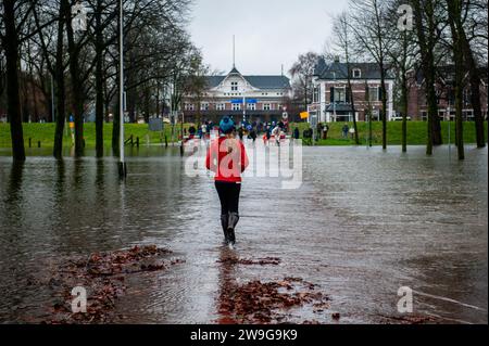 Deventer, Niederlande. Dezember 2023. Eine Frau wird durch einen überfluteten Park laufen gesehen. Aufgrund des steigenden Wassers in der IJssel stellt die Gemeinde Deventer Sandsäcke an den Kai, um die Altstadt zu schützen. Der starke Regen, der in den letzten Monaten gefallen ist, kombiniert mit der Tatsache, dass die Alpen für diese Jahreszeit ungewöhnlich warm sind, hat die IJssel in Overijssel, Gelderland, Drenthe, Brabant und Limburg überschwemmt. Quelle: SOPA Images Limited/Alamy Live News Stockfoto