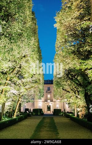 Breiter Weg zwischen den grünen Büschen des Parks zur antiken Villa am Abend Stockfoto