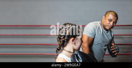 Horizontales Foto hübsches junges kaukasisches Mädchen mit schwarzen Handschuhen, schwarzer Strumpfhose und weißem Oberteil, das Boxen mit ihrem schwarzen mittelerwachsenen Lehrer lernt Stockfoto