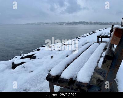 Eine Parkbank auf einer schneebedeckten Küste mit Blick auf den ruhigen Ozean Stockfoto