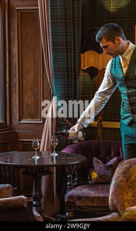 Der Kellner gießt Single Malt Whisky aus einer Flasche in das Glas auf dem Tisch. Stockfoto